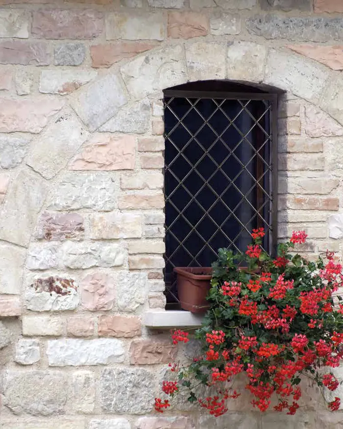 Finestra in pietra con grata di sicurezza e gerani rossi sul davanzale