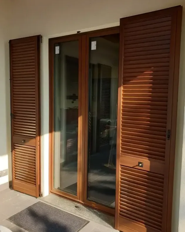 Portafinestra con persiane in alluminio effetto legno aperte su un balcone